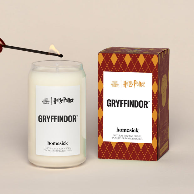 A lit Gryffindor Homesick candle displayed next to its boxed packaging on a dark cream background.