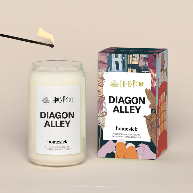 A lit Harry Potter Diagon Alley Homesick candle displayed next to its boxed packaging on a dark cream background.