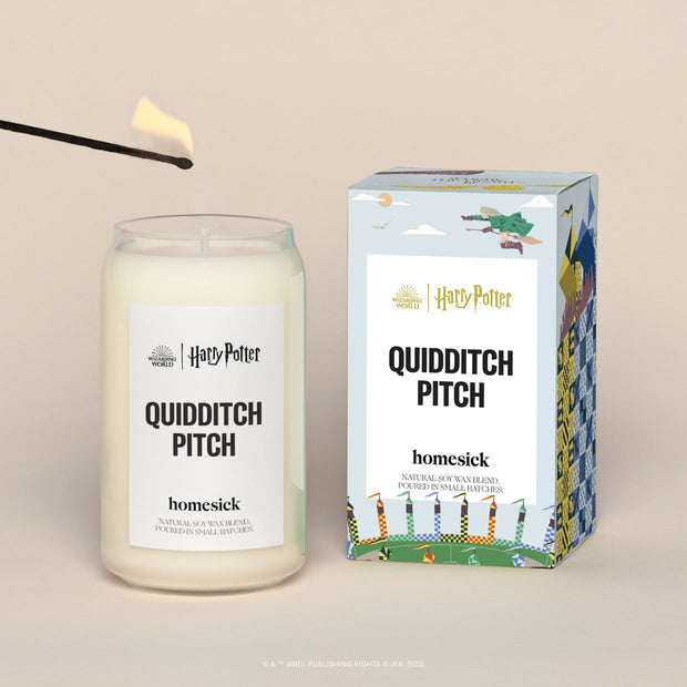 A lit Quidditch Pitch Homesick candle displayed next to its boxed packaging on a dark cream background.