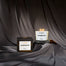 A product shot of the 3-wick Hogwarts candle and its packaging displayed on a dark silk fabric.