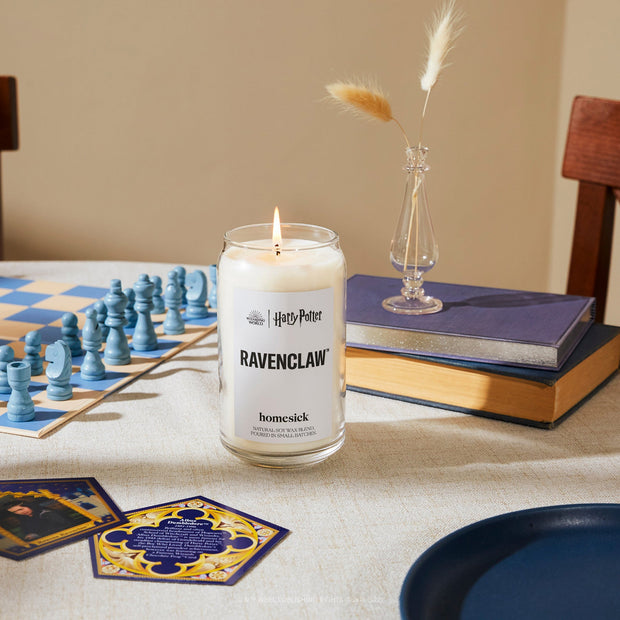A Harry Potter lifestyle shot of the Ravenclaw Candle on a dining room table. There are various Ravenclaw inspired props also on the table.