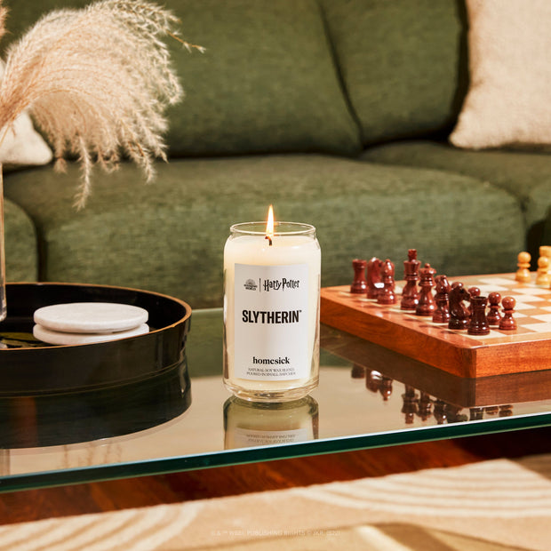 A closeup of the Slytherin Candle on a glass mirror surface next to a chess board and a large round decor tray.