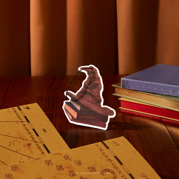 The Sorting Hat Air Freshener next to a few harry potter inspired books and papers on a wooden table.