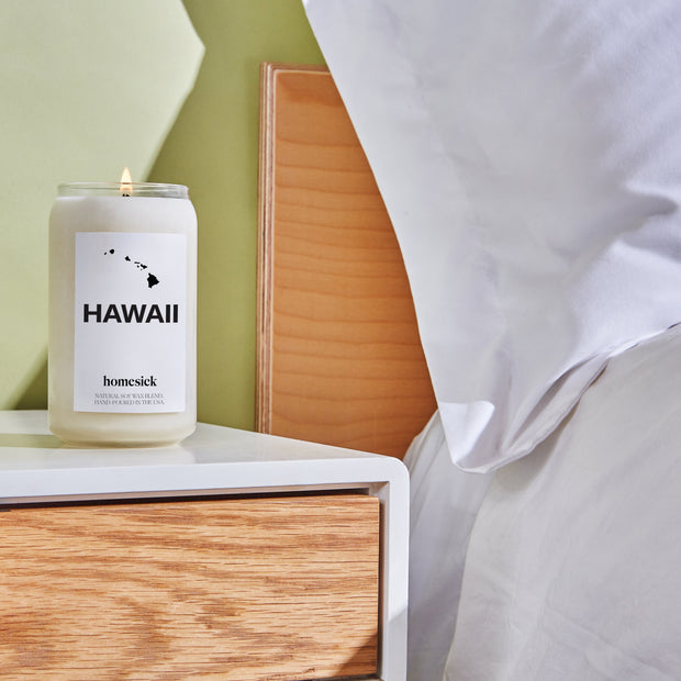 The lit Hawaii candle on a nightstand next to a cozy bed.