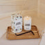 A three quarters shot of a lit Home Office Candle, its packaging and a wick trimmer on top of a wooden decor tray. They are shot on a cream linen surface.