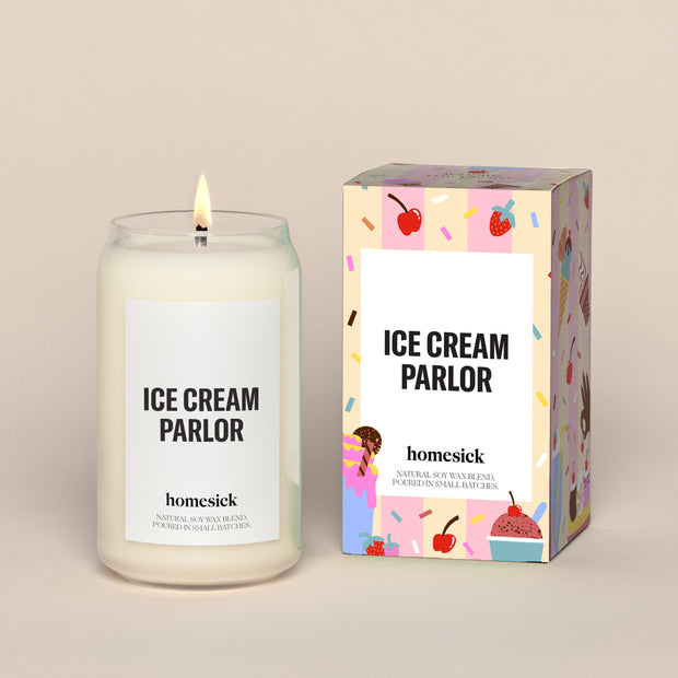 A lit Ice Cream Parlor Homesick candle displayed next to its boxed packaging on a dark cream background.
