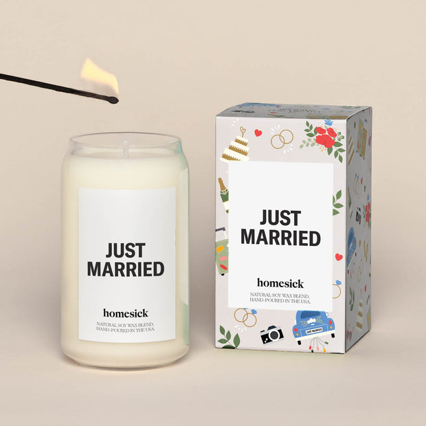 A lit Just Married Homesick candle displayed next to its boxed packaging on a dark cream background.