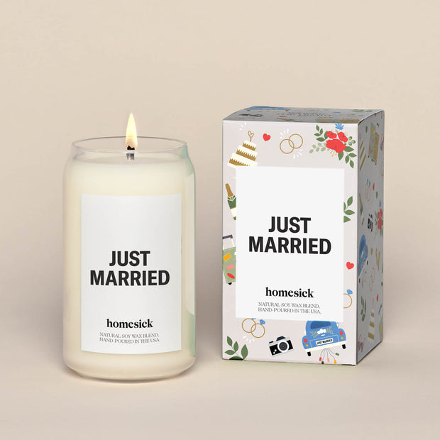 A lit Just Married Homesick candle displayed next to its boxed packaging on a dark cream background.