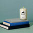 A stack of three books laying down on a seafoam green surface with a Kentucky candle propped on top.