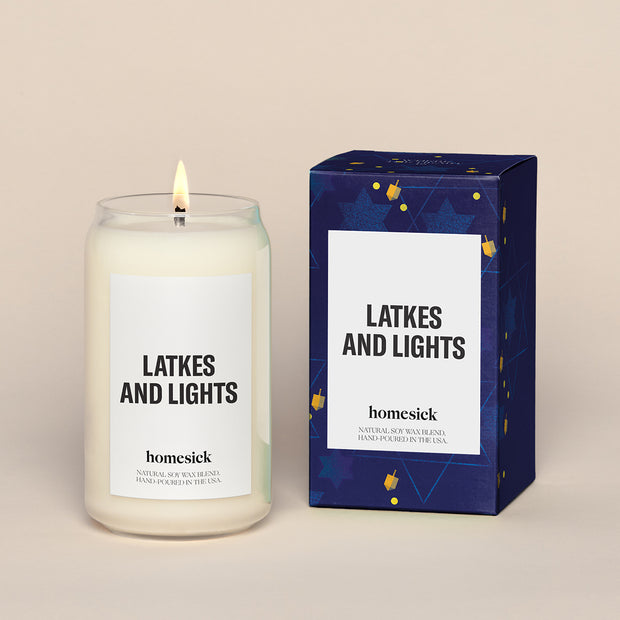A lit Latkes and Lights Homesick candle displayed next to its boxed packaging on a dark cream background.