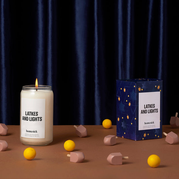 On the left, the Latkes and Lights candle with the packaging on the right. They are displayed on a light brown surface that has dreidels and balls on it.