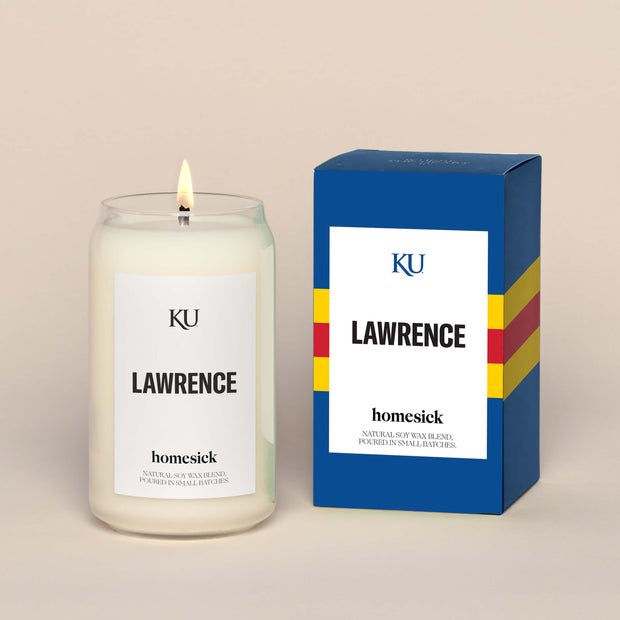 A lit Lawrence Homesick candle displayed next to its boxed packaging on a dark cream background.