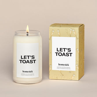 Single Lets Toast Candles next to a the gold box with animated Champagne glasses over all print. There is a white label that reads 