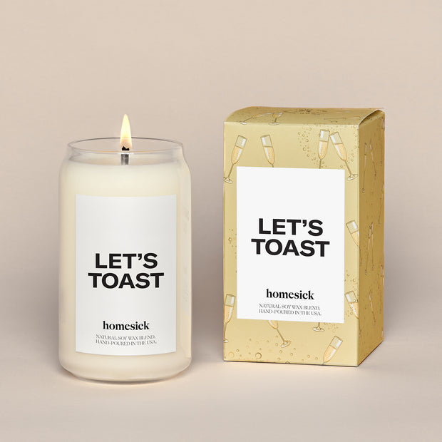Single Lets Toast Candles next to a the gold box with animated Champagne glasses over all print. There is a white label that reads "Lets Toast"  