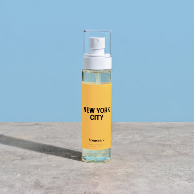 Another product shot of the New York City Room Spray displayed on a smooth concrete surface with a light blue background.