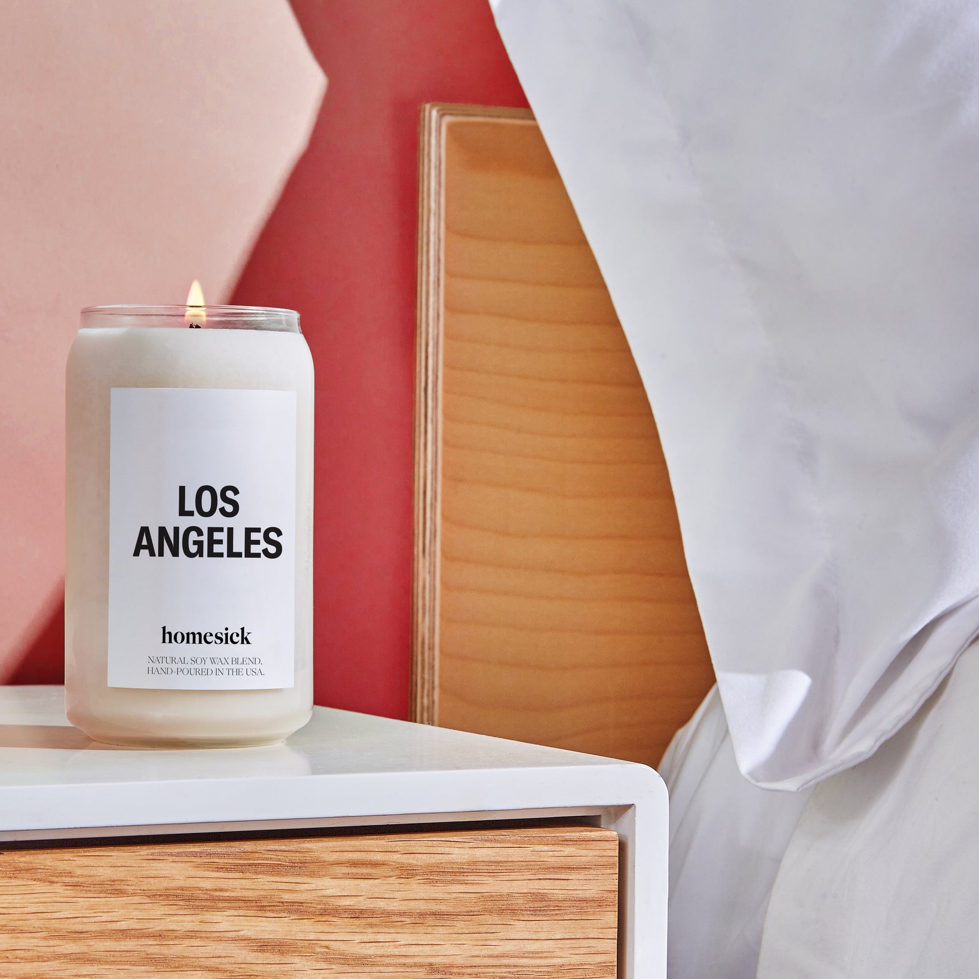 A bedside shot of the Los Angeles candle on a white night stand that has a wooden drawer.