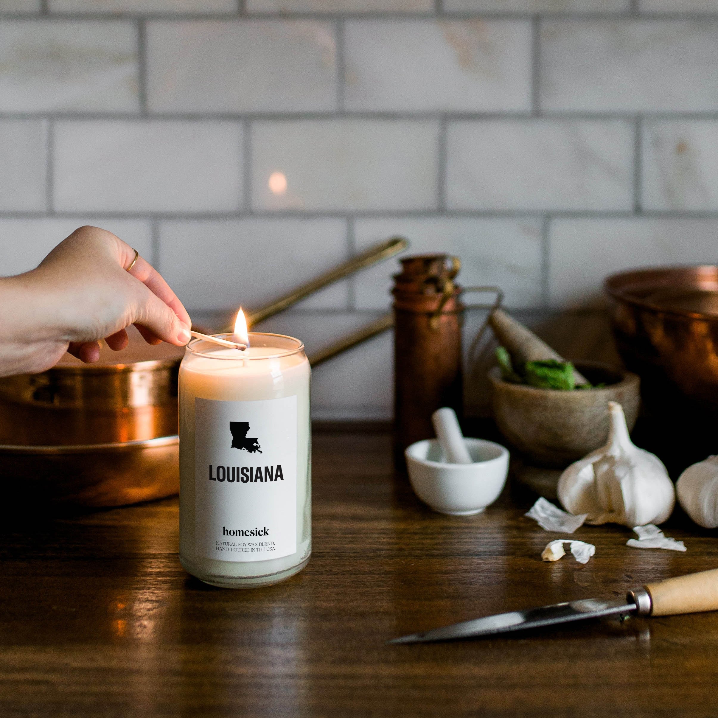 A hand going to lit the Louisiana homesick candle while in the kitchen space.