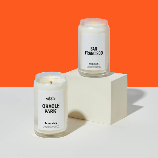 The San Francisco and Oracle Park Candles on top of white pedestals that are on a white surface with a neon orange background.