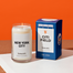 The New York City Candle next to the CIti Field packaging displayed on a white surface with burnt orange background.