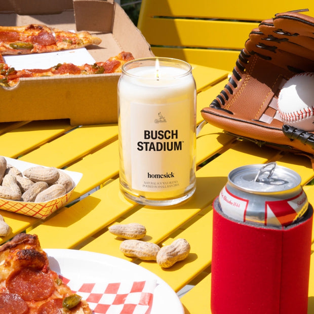 A lifestyle image of the Busch Stadium candle in the center of a close up shot of a baseball picnic.
