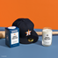 A stylized shot of the Minute Maid Park candle and its packaging on a blue surface with an orange background. There is a baseball bat and hat as props around the candle.