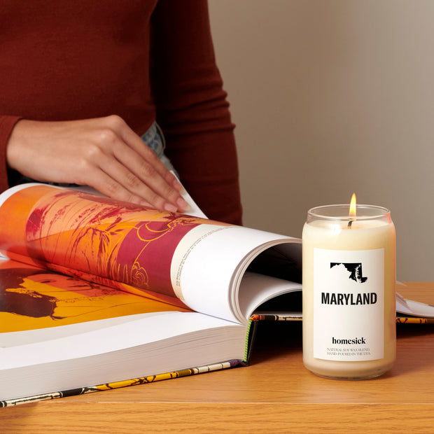A shot of someone reading a art book with a lit Maryland candle in front of it.