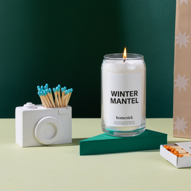 A camera match holder next to the Winter Mantel Candle. 