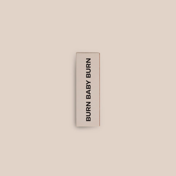 A product shot of the top of the Homesick matches displayed on top of a cream background. The box reads, "burn baby burn."