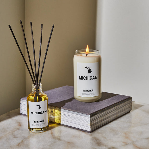 On top of a marble surface left to right is the Michigan reed diffuser, a large book and a Michigan table on top of that. 