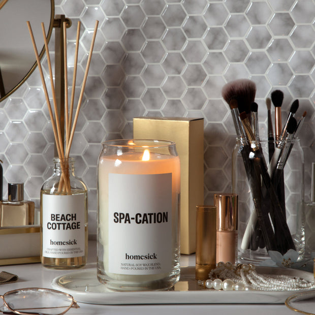 Lit spa-cation candles next to a beach cottage reed diffuser on a vanity with a calm setting.
