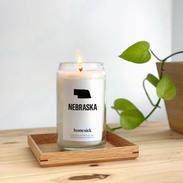 A close up of the Nebraska candle displayed in a wooden tray on top of a wooden surface.