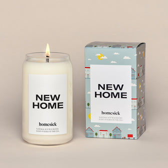 New Home Candle next to the packaging. Packing is a soft blue box with animated overall print of different homes.