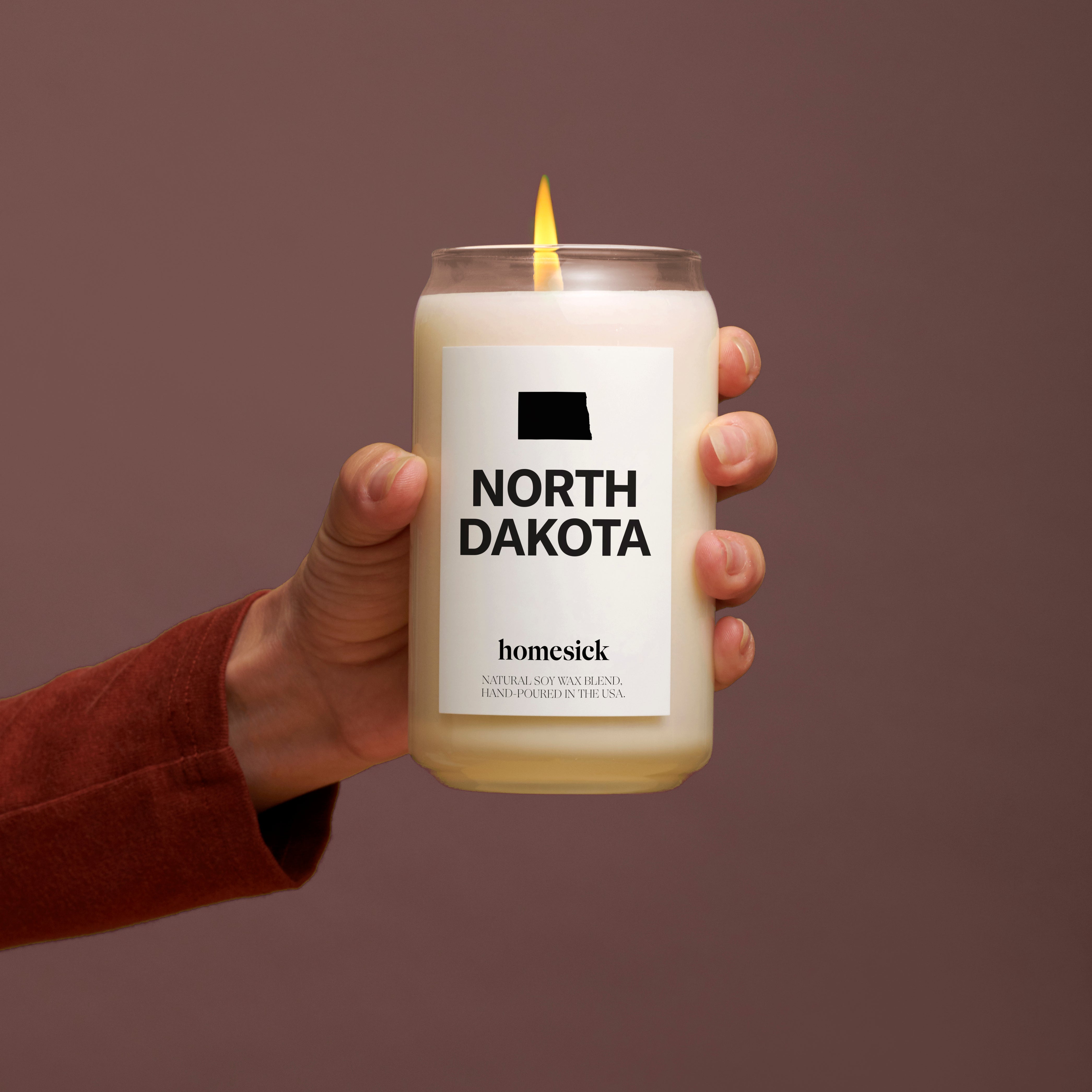 A hand holding a North Dakota candle in front of a deep purple wine background.