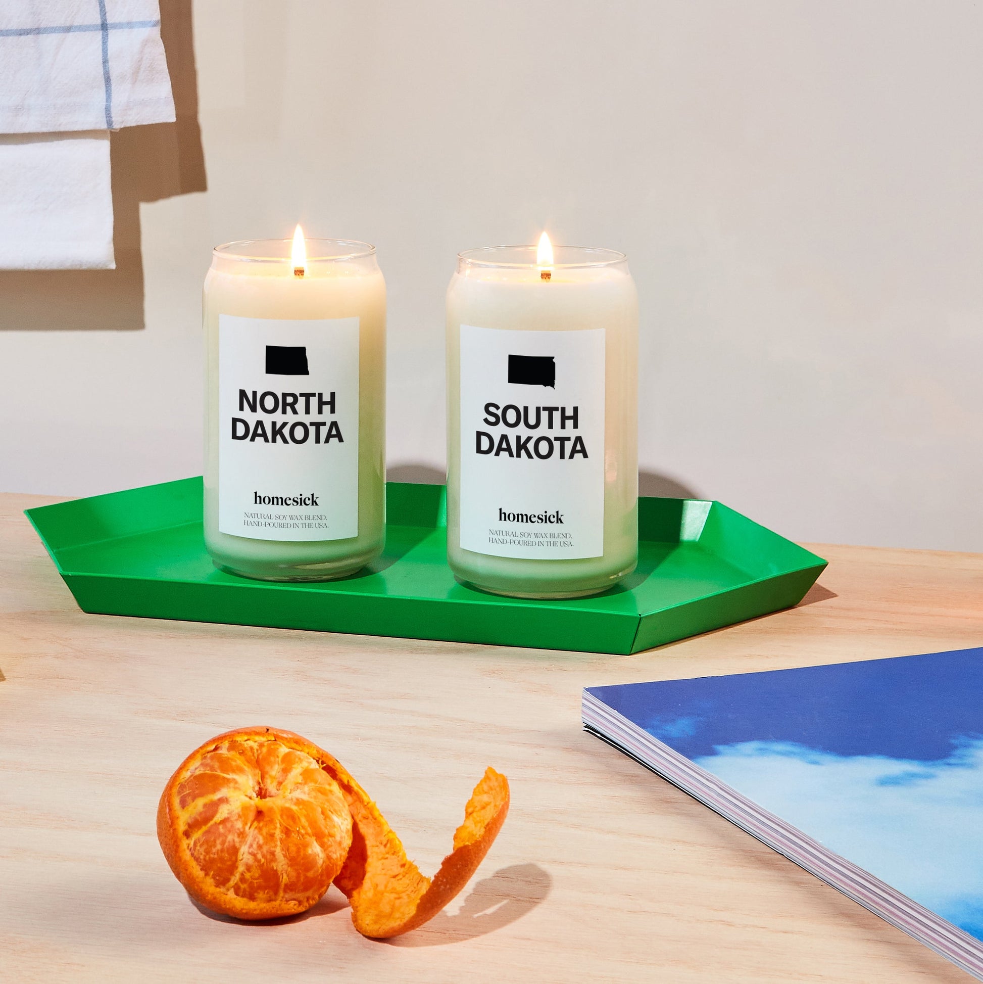 The North Dakota and South Dakota candles displayed on a green decor tray that sits on a light wood surface.