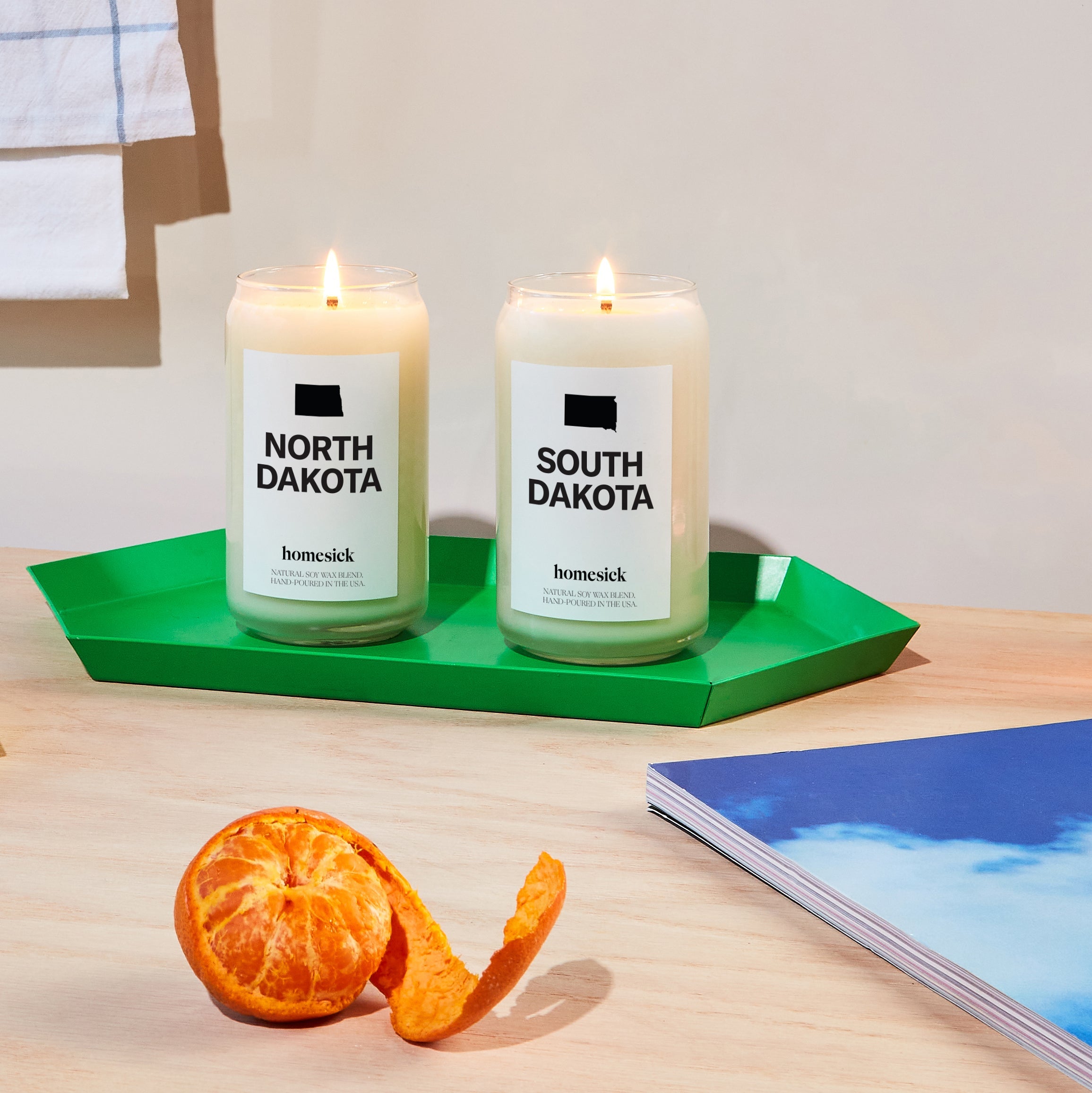 The North Dakota and South Dakota candles displayed on a green decor tray that sits on a light wood surface.