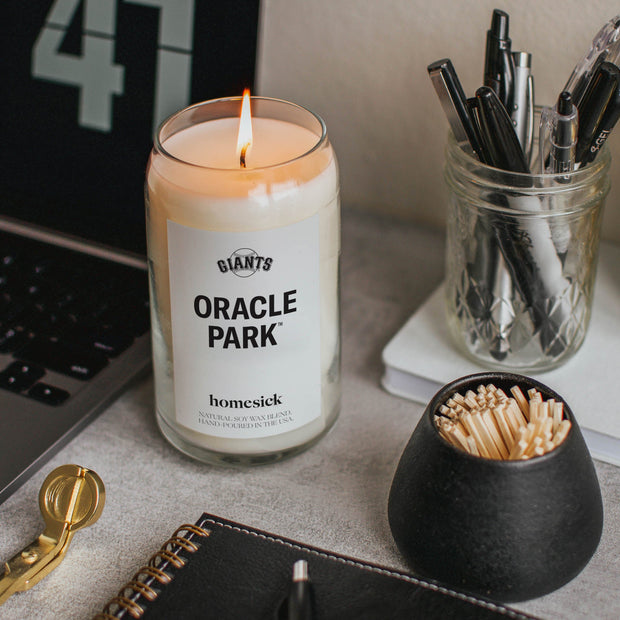 A close up of the Oracle Park candle that is next to a laptop within someone's workspace.