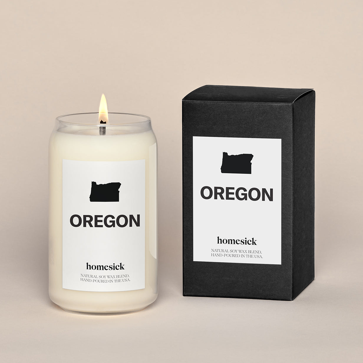 A lit Oregon Homesick candle displayed next to its boxed packaging on a dark cream background.