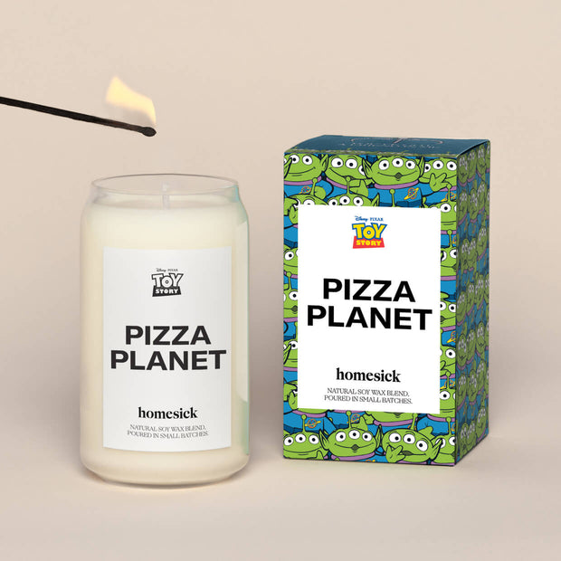 A lit Pizza Planet Homesick candle displayed next to its boxed packaging on a dark cream background.