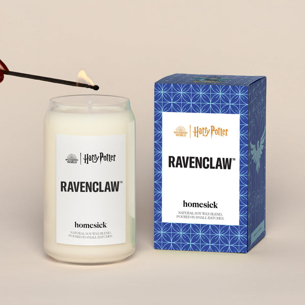 A lit Ravenclaw Homesick candle displayed next to its boxed packaging on a dark cream background.