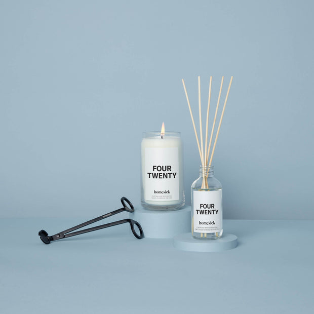 Shot in a light blue studio, there is the Four Twenty Candle on a tall pedestal and a Four Twenty Reed Diffuser on a shorter pedestal.
