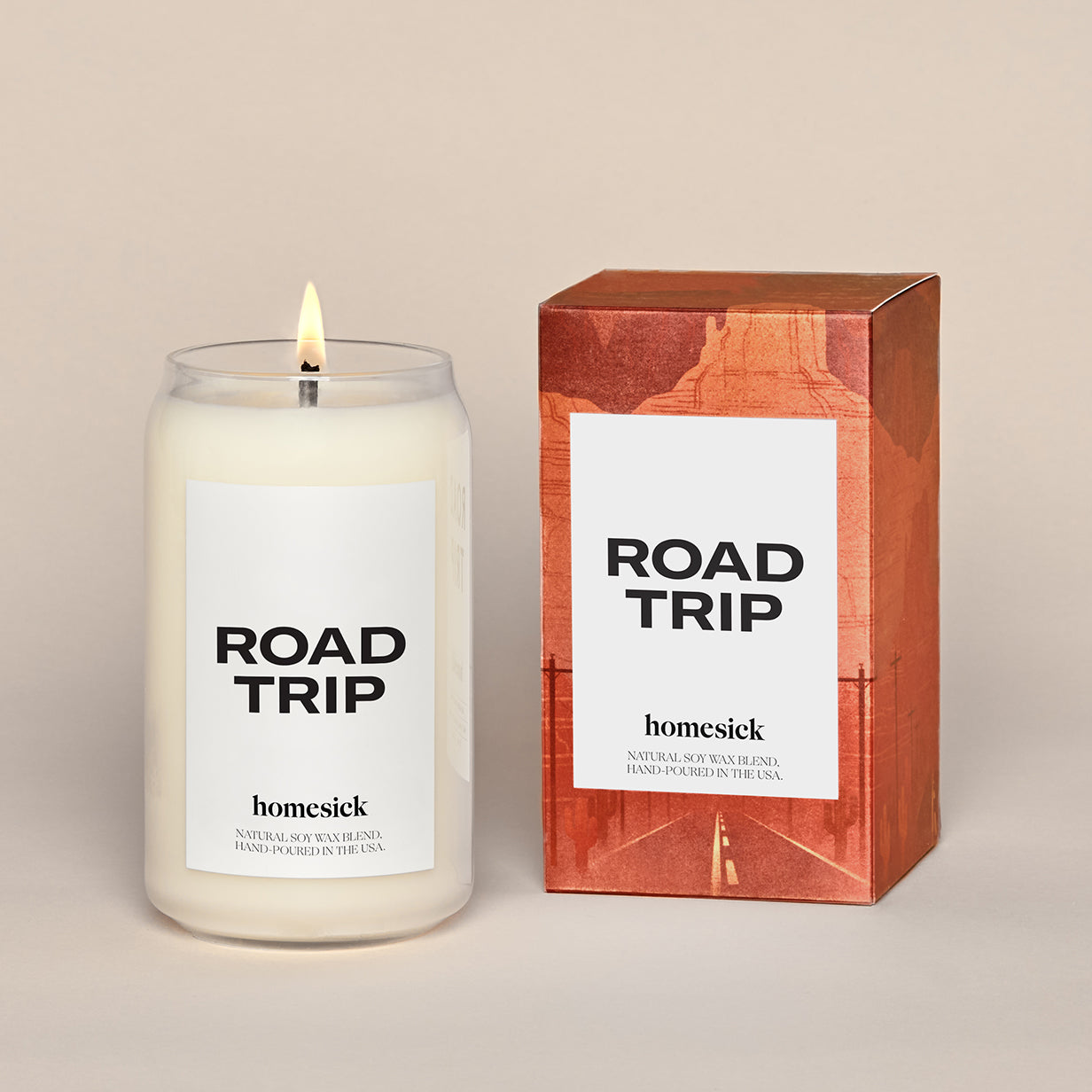 A lit Roadtrip candle sitting next to the a graphic packaging box.