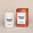 A lit Road Trip Homesick candle displayed next to its boxed packaging on a dark cream background.