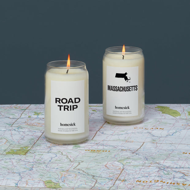 A lit Roadtrip candle next to a lit Massachusetts candle on a map.