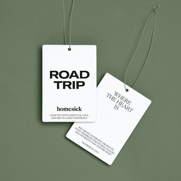 Two Road Trip Car Fresheners displayed on an everest green background. One Freshener shows the front side and the other shows the backside.