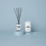 The Northern California reed diffuser next to the San Francisco candle that are in a light blue studio environment.