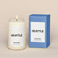 A lit Seattle Homesick candle displayed next to its boxed packaging on a dark cream background.