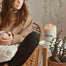 A lifestyle image of the Seattle Candle on a white round side table with a woman drinking a glass of tea in the background.