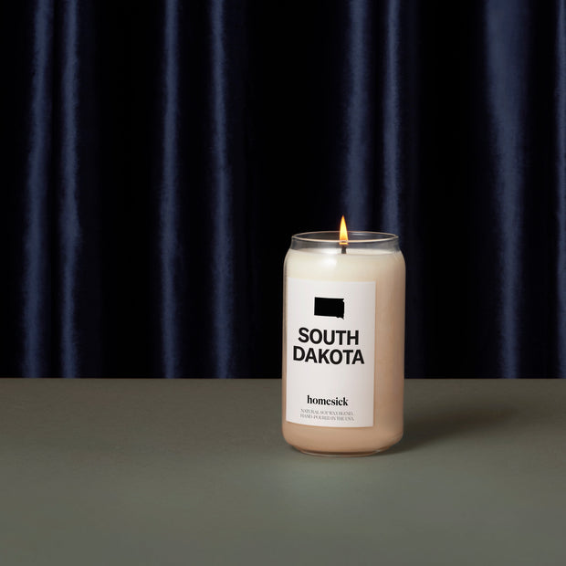 The South Dakota candle on a dark gray surface with a navy silk curtain as the background.
