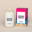 A lit Spring Break Homesick candle displayed next to its boxed packaging on a dark cream background.