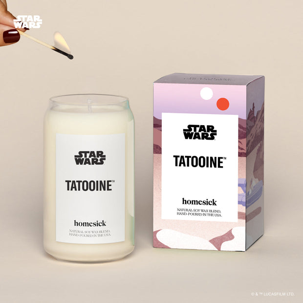 A lit Star Wars Tatooine Homesick candle displayed next to its boxed packaging on a dark cream background.